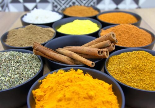 Colorful assortment of spices in bowls with cinnamon sticks on a wooden surface.